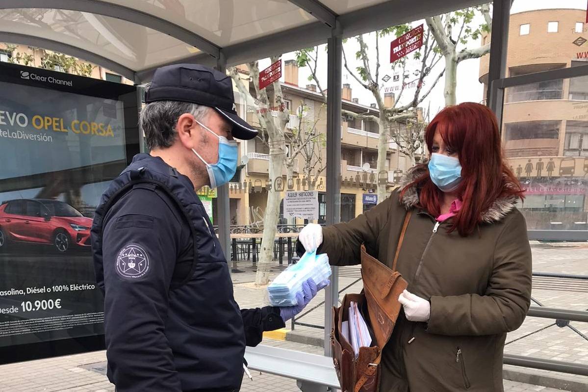 Un miembro de la policía local entregando una mascarilla a una vecina.