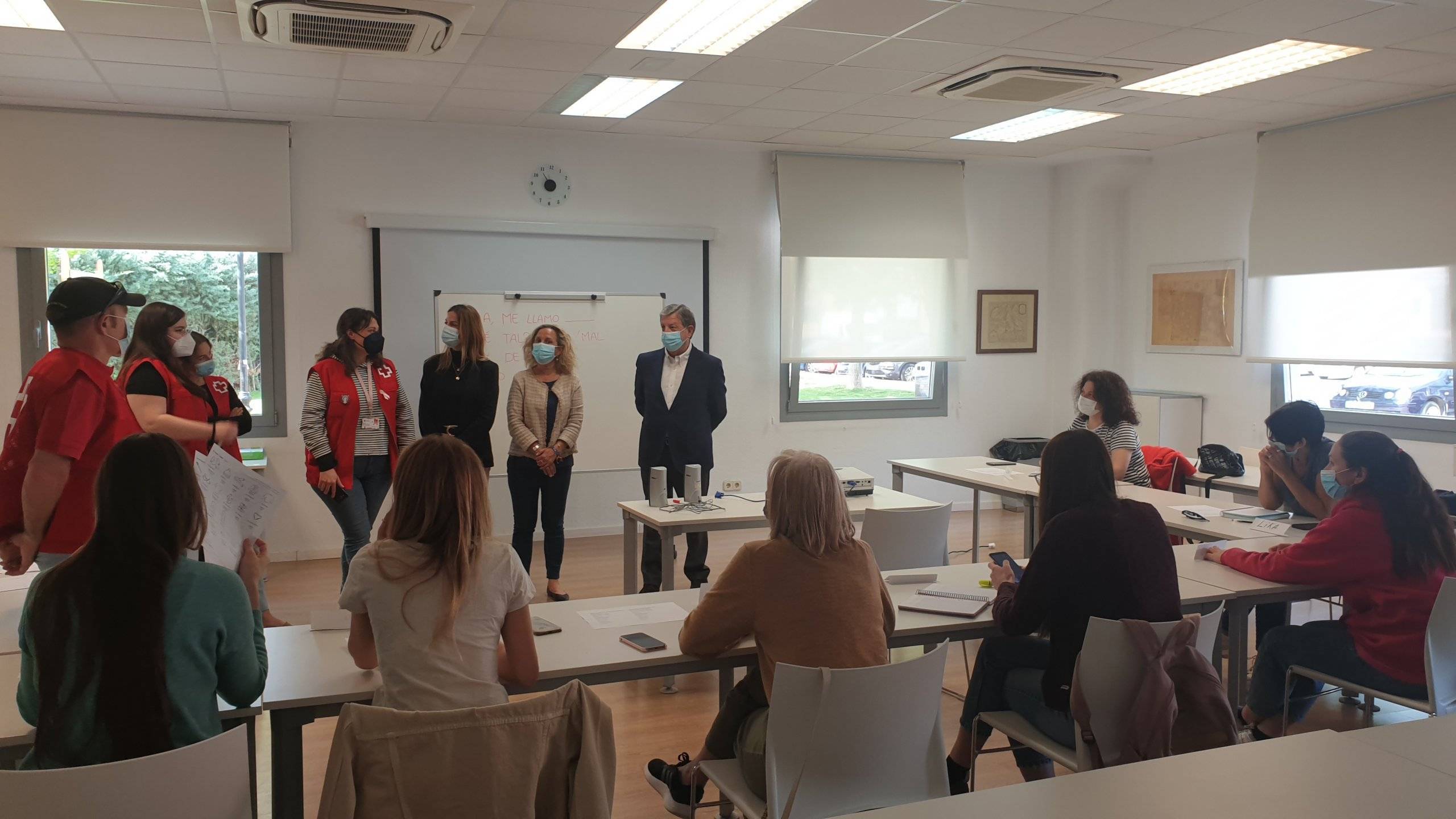 Autoridades locales y miembros de Cruz Roja, de pie, en un aula junto a alumnos sentados.