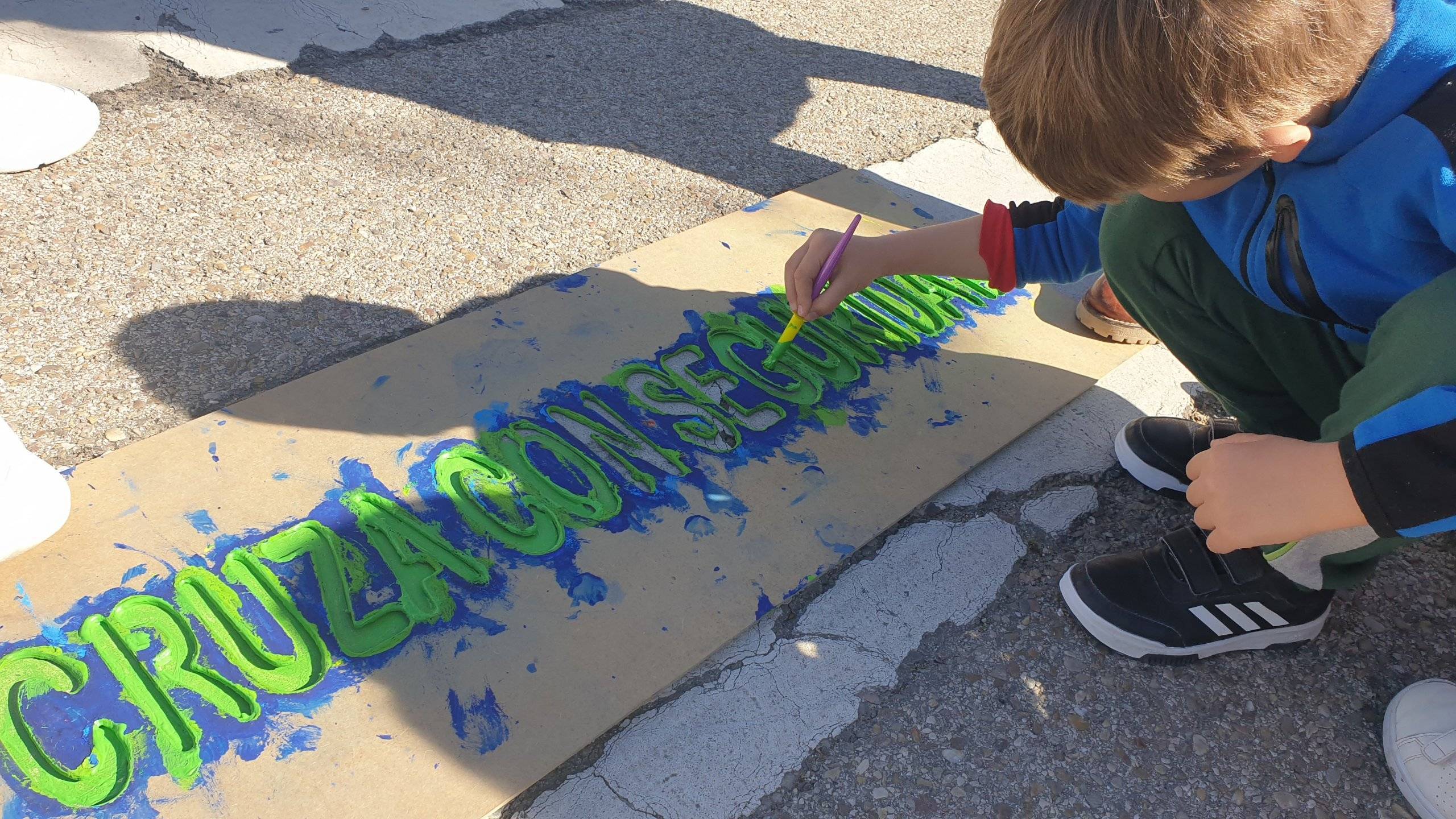 Niño pintando en un paso de peatones un mensaje de seguridad vial.