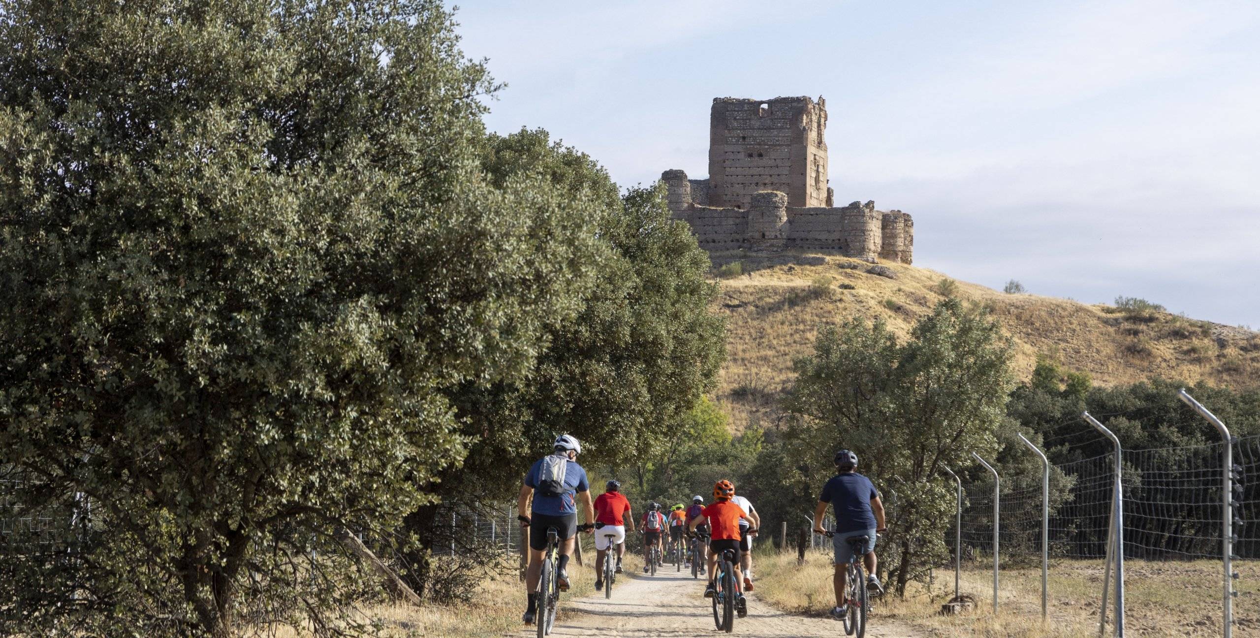 Grupo de personas en bicicleta por el campo y al fondo un castillo