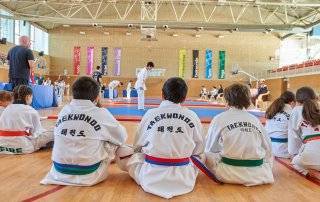 Participantes del Campeonato de Taekwondo mirando a otros deportistas mientras realizan su ejercicio.
