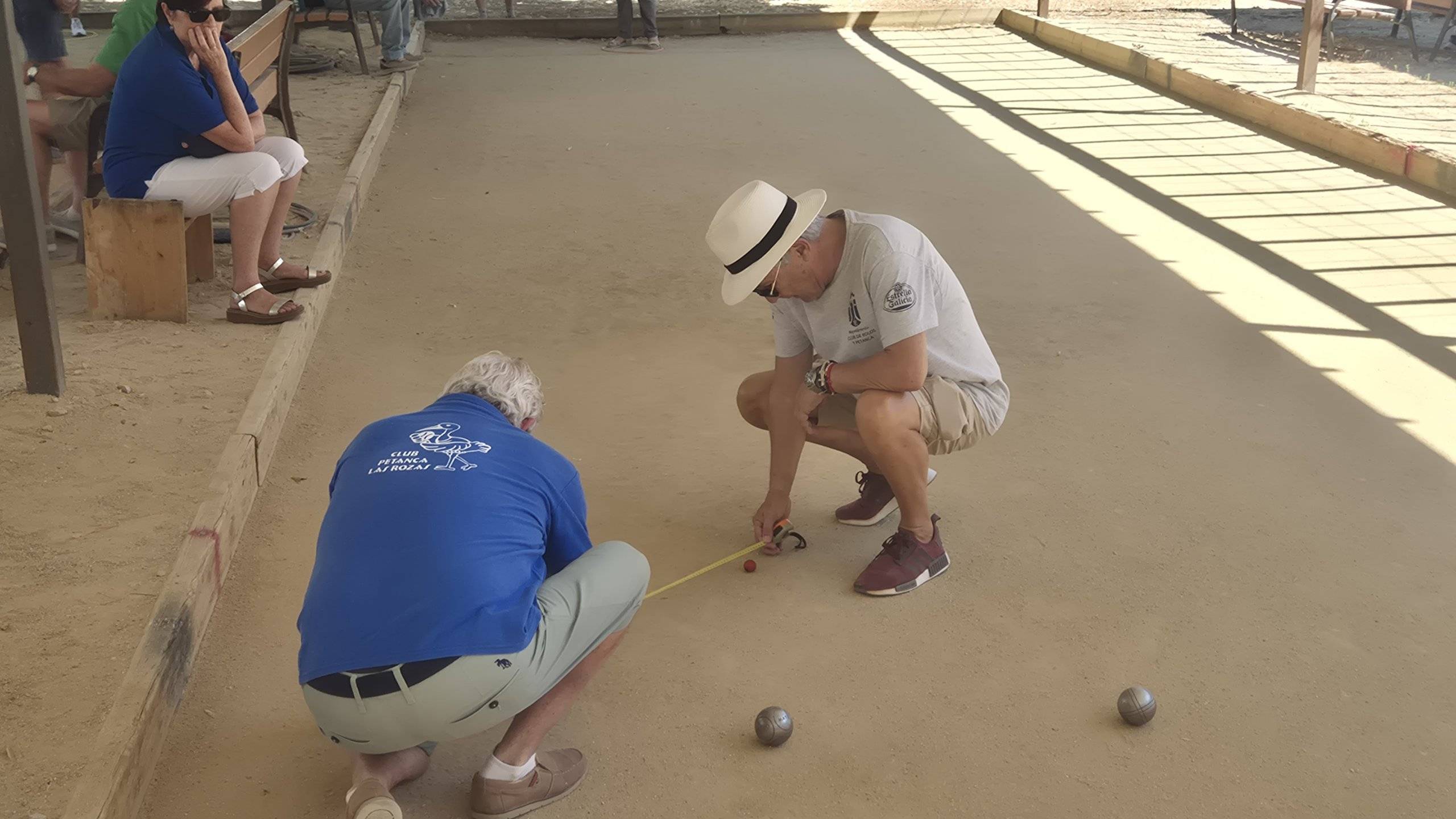 Dos jugadores miden la distancia de las bolas de petanca.