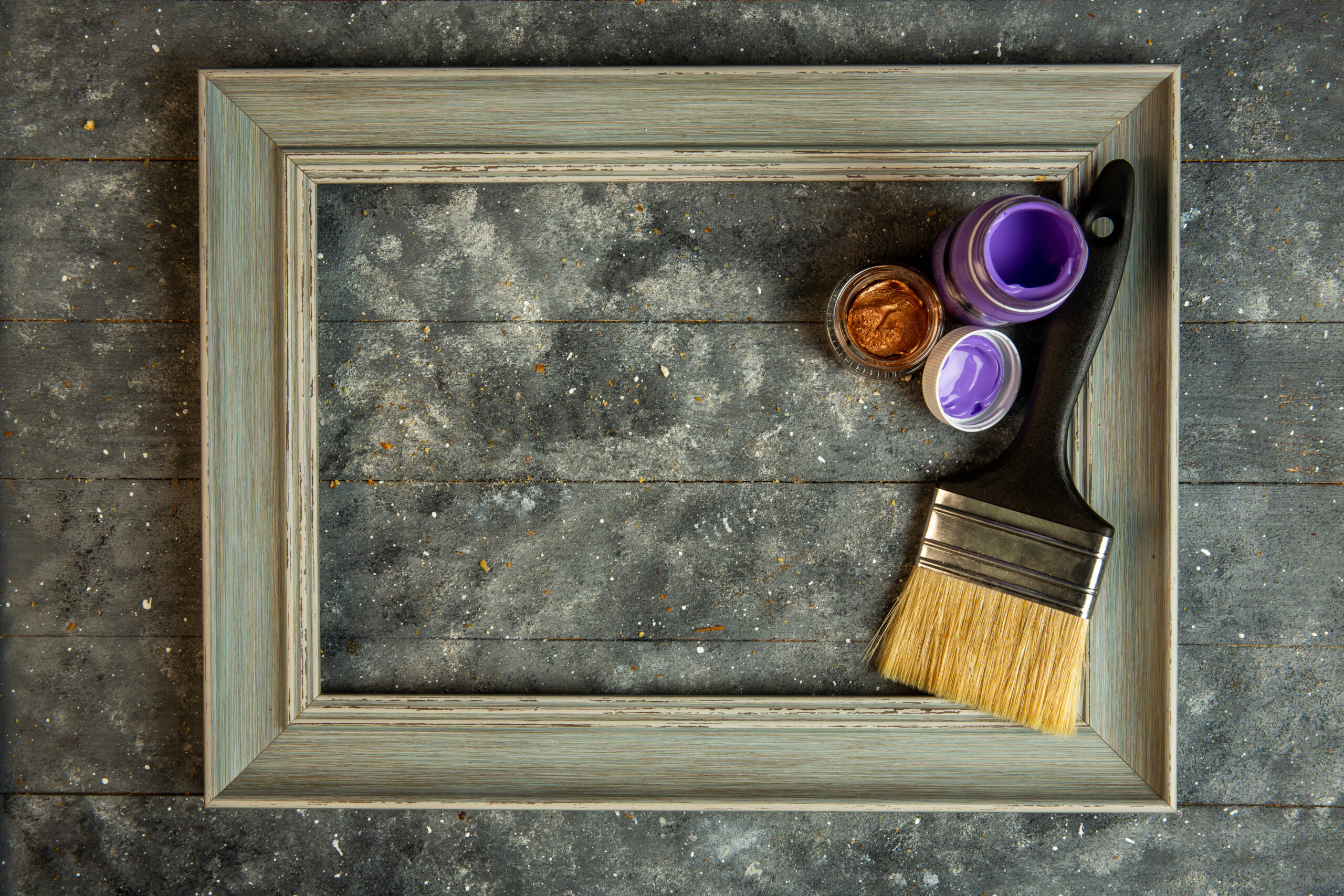 top view of empty wooden picture frame with acrilic paints and paint brush on rustic background