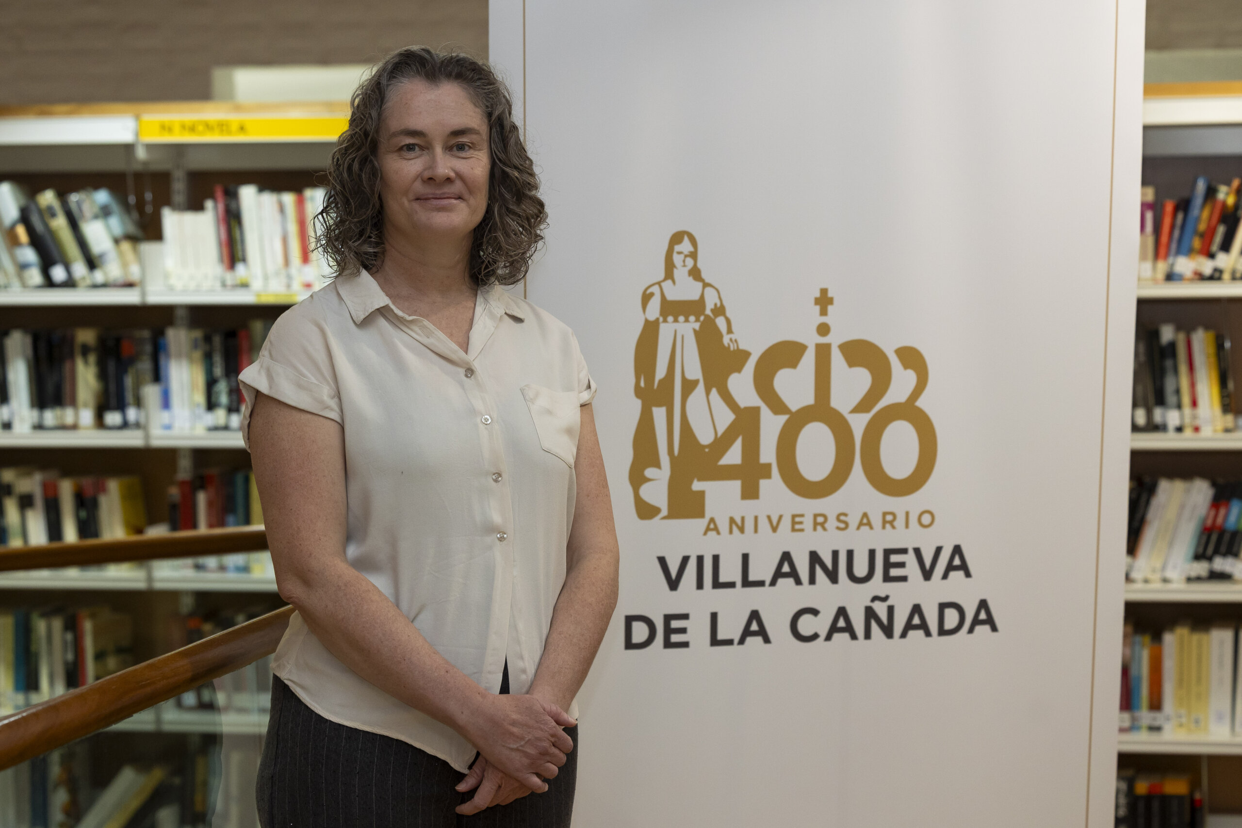 La presidenta de la Asociación Histórica Aulencia junto al logotipo del 400.º aniversario de la concesión del título de villazgo a Villanueva de la Cañada.