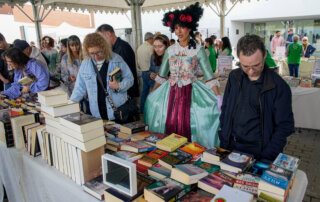 Público mirando los puestos de libros, junto a una actriz del teatro de calle.