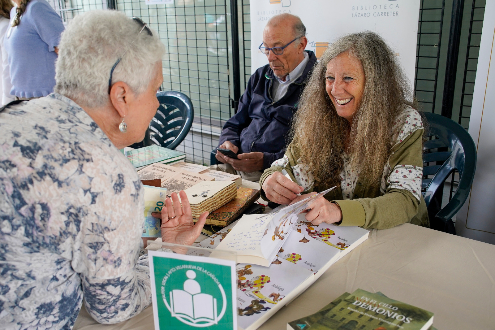 Una de las autoras locales firma un ejemplar de su obra a una asistente al Mercadillo Solidario de Libros.