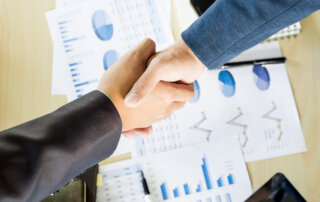 Dos personas se dan la mano sobre unos gráficos económicos.